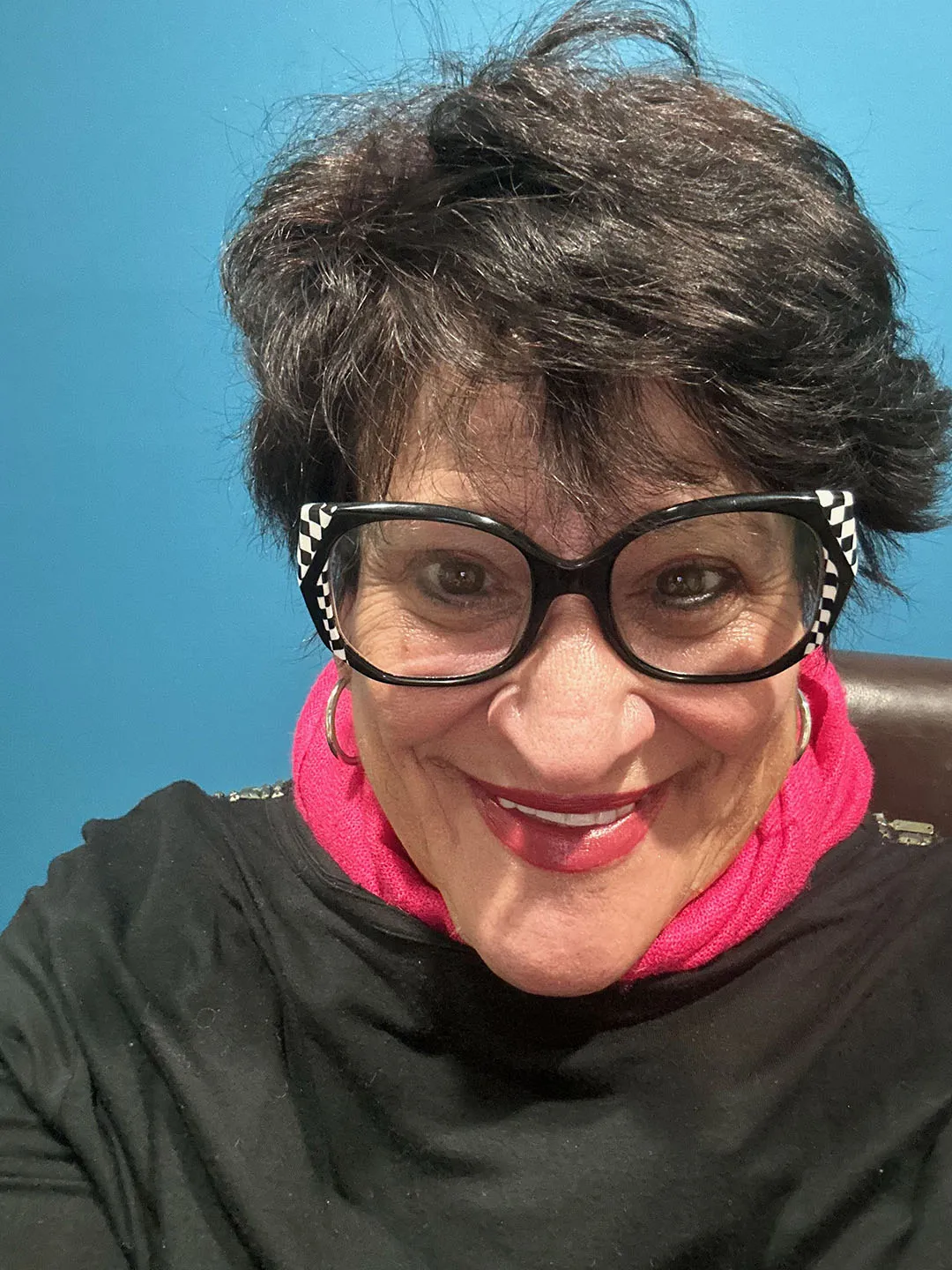 A woman wearing stylish power glasses and a black shirt, smiling and looking directly at the camera.